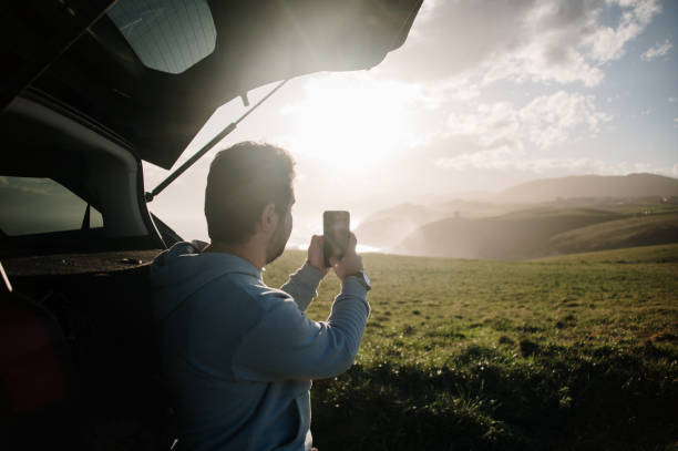istock Young man taking a picture with a smart phone by his car 1300288071