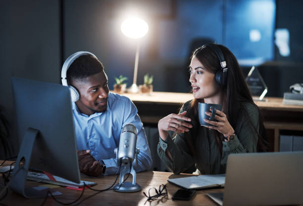 She's always up for a good debate Shot of two people doing a broadcast while sitting in an office at night radio broadcasting photos stock pictures, royalty-free photos & images