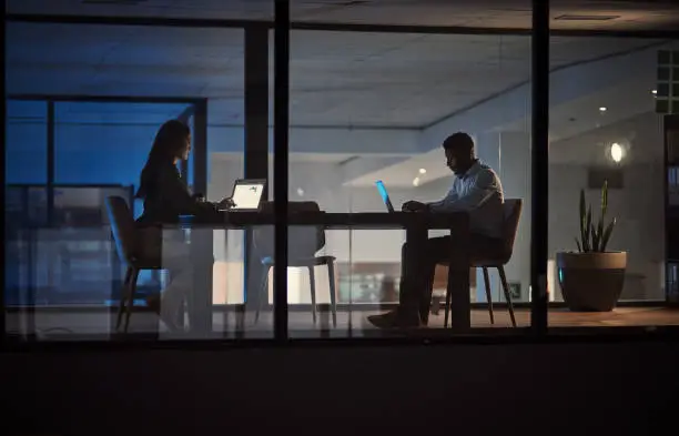 Shot of two businesspeople working on laptops in an office at night