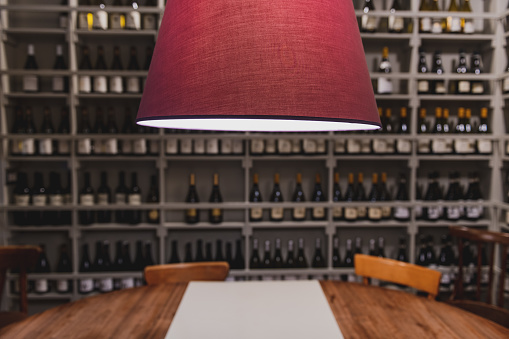 Close up on lamp in tasting room of restaurant wine shop, out of focus background with large number of wine bottles