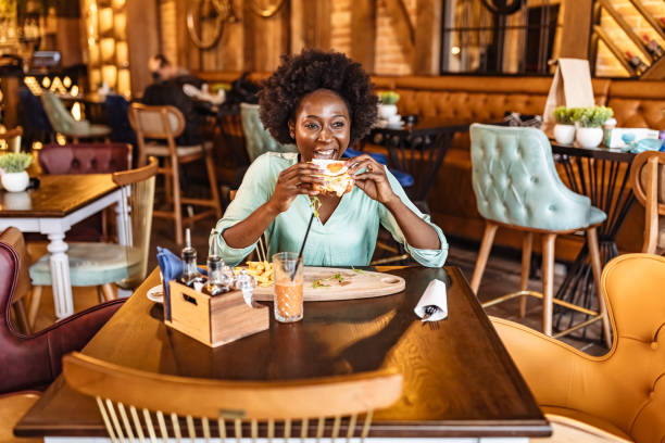 Beautiful young lady eating a tasty burger at an indoor café.