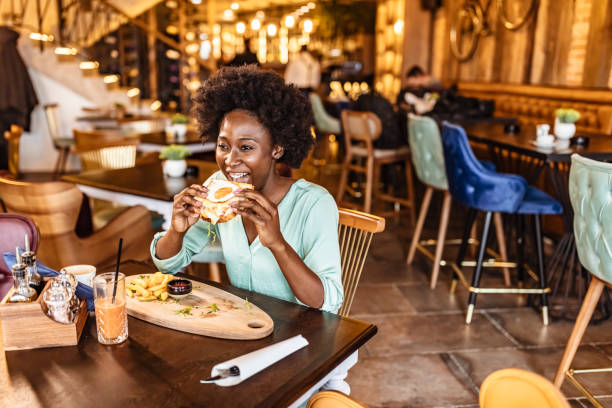One smiling African woman about to eat a meatless vegan cheese burger while sitting in modern restaurant during the day.