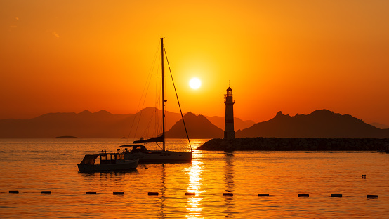 Beautiful sunset over islands in Mediterranean sea. Lighthouse and sailboats in harbor at sunset. Bodrum, Turkey.