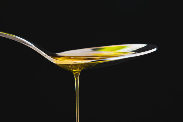 olio d'oliva liquido su un cucchiaio su sfondo nero. cucina - cooking oil olive oil nutritional supplement spoon foto e immagini stock