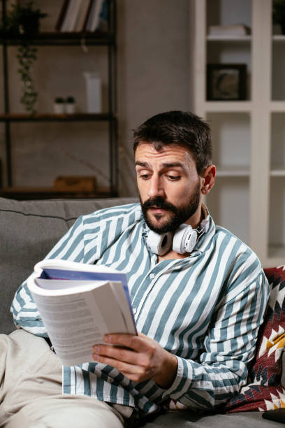 istock Young man reading a book on the couch. 1300294287