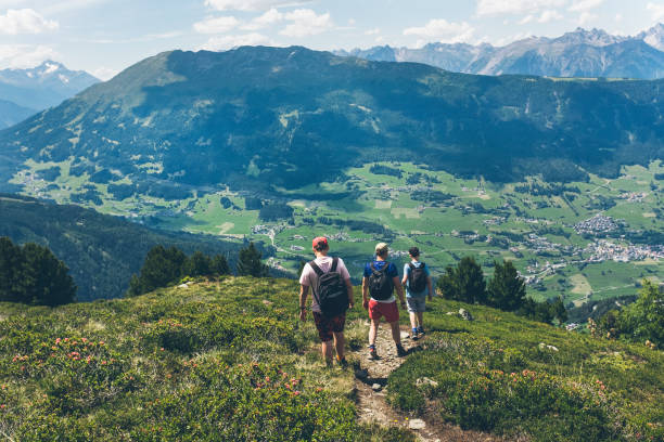 Teenager boys and a father walking on the path in the mountains in summer - spending vacations outdoors, living healthy, with breathtaking mountains and valley views and panorama. stock photo