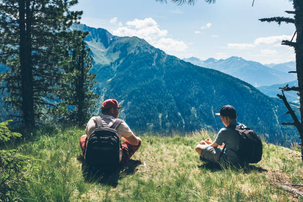 deux garçons adolescents, frères, amis, assis sur le rebord de la montagne, clairière, pré haut dans les montagnes, prendre une pause, se reposer, parler, profiter de leur journée de randonnée d’été, se lier, vivre en bonne santé. - european alps austria mountain tirol photos et images de collection