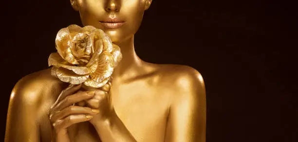 Golden Makeup Skin Fashion Model. Close up Woman Glowing Face Perfect Portrait with Gold Rose Jewelry. Bodyart Painting. Black Studio Background