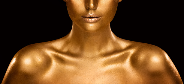 Fashion Gold Skin Beauty Woman Portrait. Close up Face Model Golden Makeup. Gold Lips Make up and Shiny Body Paint over Black Studio Baclground