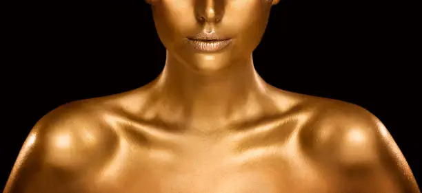 Fashion Gold Skin Beauty Woman Portrait. Close up Face Model Golden Makeup. Gold Lips Make up and Shiny Body Paint over Black Studio Baclground
