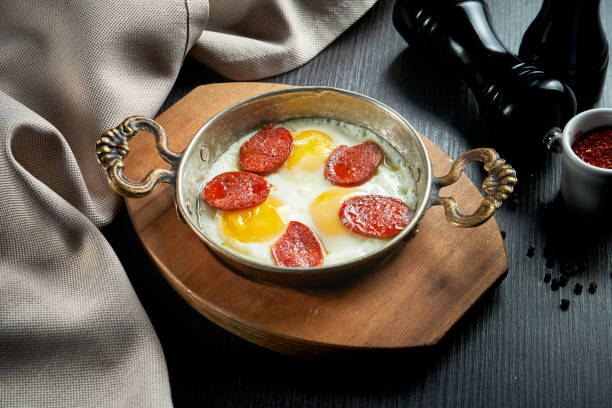 istock Appetizing turkish breakfast dish - scrambled eggs with sujuk in a frying pan on a black background 1300299148