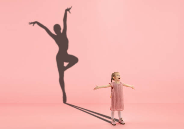 子供の頃と大きくて有名な未来を夢見る。コーラルピンクの背景にフィット女性バレエダンサーの女の子と影と概念的なイメージ - motion muscular build dancing ballet ストックフォトと画像