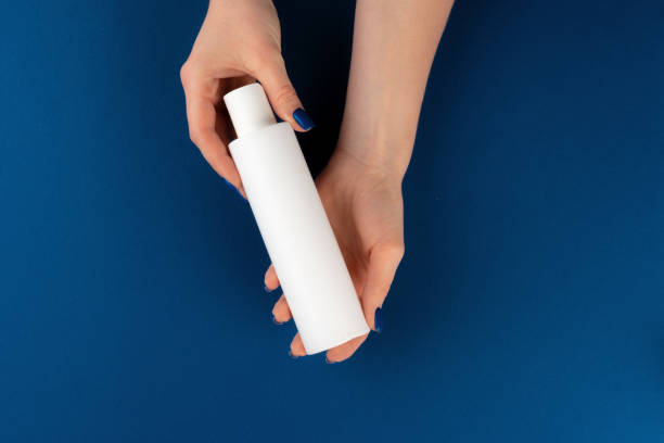 istock Female hands holding cosmetics container in hands against blue background 1300306845