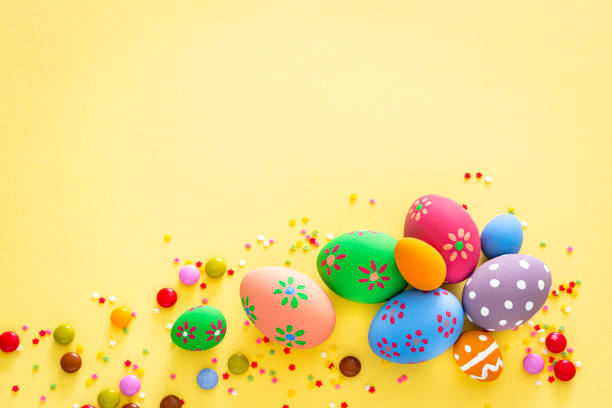 istock Colorful Easter eggs with candies and sugar sprinkles on yellow background. Copy space 1300309780