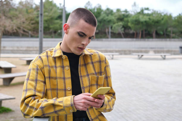 joven guapo que usa maquillaje, charlando en su teléfono inteligente molesto. tipo no binario andrógino. - non verbal communication fotografías e imágenes de stock