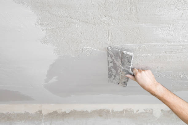 istock Young adult man hand using spatula and plastering ceiling with fresh finishing putty. Closeup. Repair work of home. View from below. 1300310121