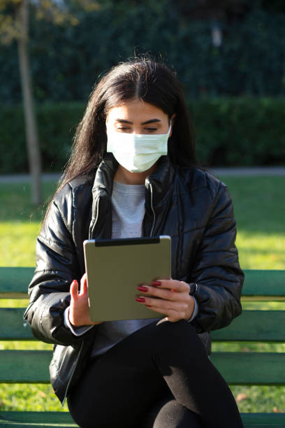 istock Young woman sitting on a bench in a public park using digital tablet 1300311417