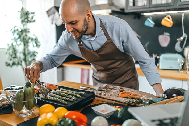 young man roasting salmon steaks and asparagus on an electric grill - prepared fish seafood barbecue grilled imagens e fotografias de stock