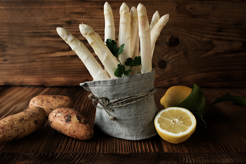 Bundle of fresh white asparagus and ingredients on rustic wood. Food photography with short deep of focus. Background for nutrition and gastronomy concepts with space for text.