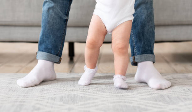 istock Father Helping Baby Toddler Make First Steps Standing Indoors, Cropped 1300315127