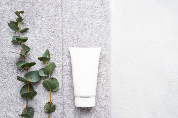 istock Rolled grey towels, body treatment mock-up, and eucalyptus branches on white concrete background. SPA concept 1300315253