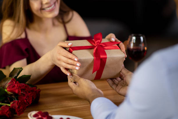 femme affectueux surprenant son petit ami noir avec le cadeau romantique pour le jour de valentine - anniversary couple rose black photos et images de collection