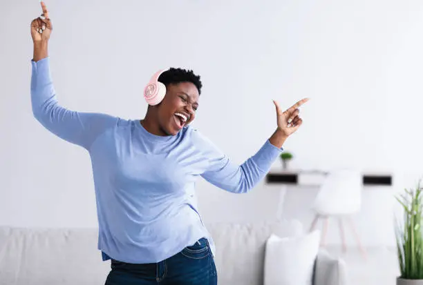 Photo of Black woman listening to music in headphones and dancing