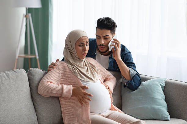 Worry Muslim Husband Calling Emergency While His Pregnant Wife Having Contractions Worry Muslim Husband Calling Emergency While His Pregnant Wife Having Prenatal Contractions At Home. Islamic Expecting Mother In Hijab Suffering Painful Spasms And Spontaneous Labour, Copy Space muscular contraction stock pictures, royalty-free photos & images