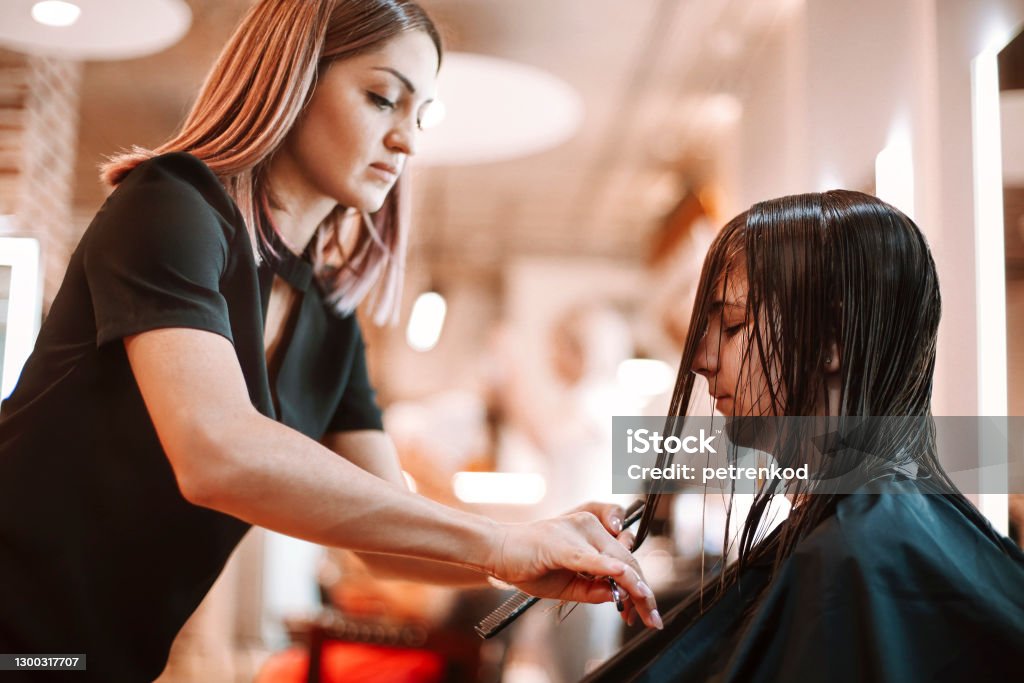 Women discussing beauty products in salon Professional beautician discussing treatment product with female client while standing near shelves with cosmetics in modern beauty salon Hairdresser Stock Photo