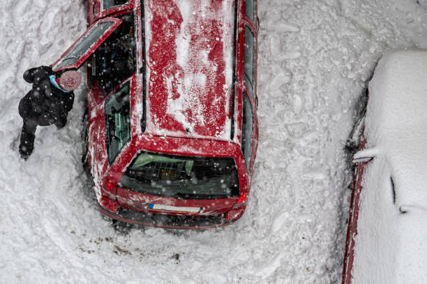 vista dall'alto donna pulizia auto rossa coperta dalla neve per guidare dopo forti nevicate blizzard - snow car window ice scraper foto e immagini stock