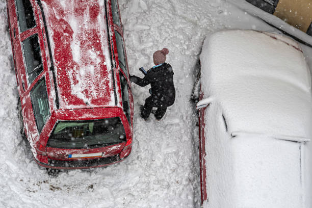 vista dall'alto donna pulizia auto rossa coperta dalla neve per guidare dopo forti nevicate blizzard - snow car window ice scraper foto e immagini stock