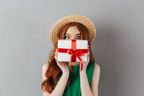 istock Shocked redhead young woman covering face with present. 1300318415