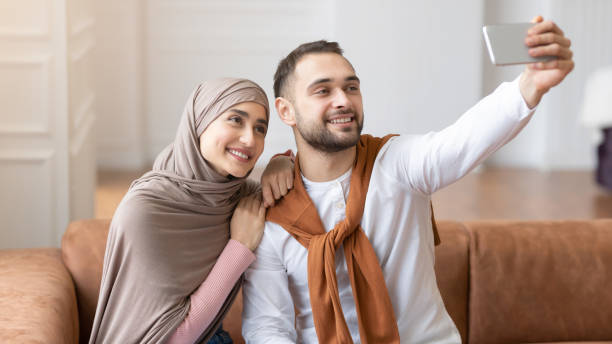istock Cheerful Muslim Spouses Making Selfie On Mobile Phone At Home 1300321669