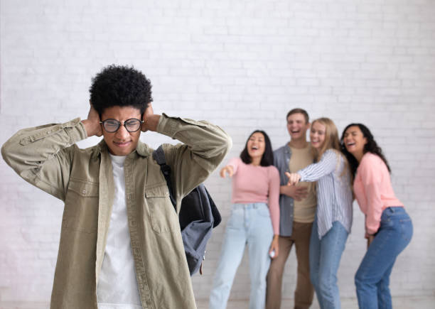 Bullying victim, depressed student suffers from school humiliation Bullying victim, depressed student suffers from school humiliation. Sad young african american guy in glasses closes ears, as not to hear laughter of international people, studio shot, empty space man closing ears photos stock pictures, royalty-free photos & images