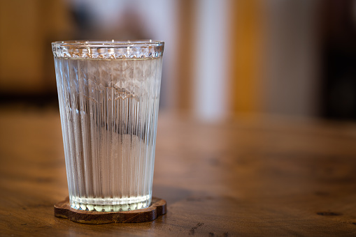 A glass of iced drinking water, placed on the oak wooden table. Close-up and selective focus photo.