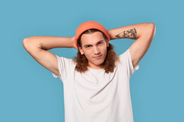 istock Freestyle. Curly-haired guy wearing hat standing isolated on blue hands behind head smiling confident close-up 1300324600