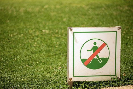 Closeup of a prohibition sign of not to walk on the grass with a sunny green lawn on background. Barcelona, Spain.