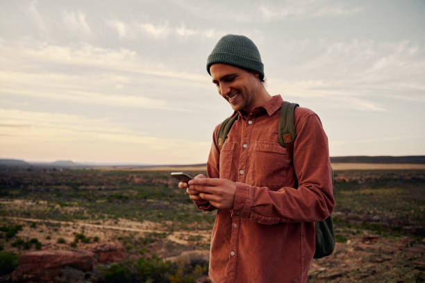 istock Happy male hiker with backpack and cap using smartphone on mountain 1300325471