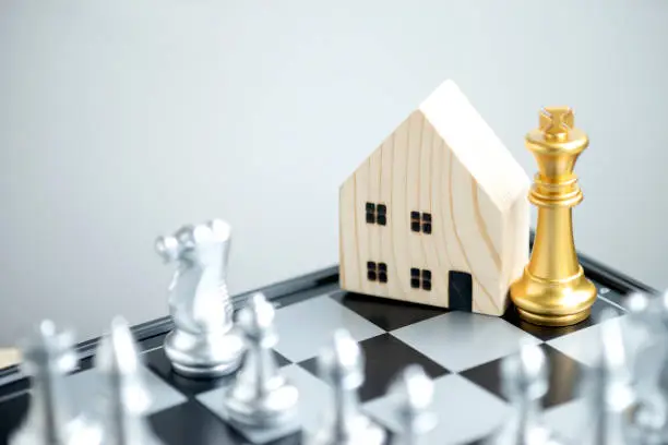Photo of Wooden house model with a gold king chess on a chessboard