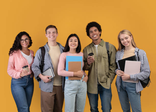 Modern students from different countries and exchange program Modern students from different countries and exchange program. Smiling young international people with cups of takeaway coffee, books and backpacks look at camera, isolated on orange background multi ethnic group college student group of people global communications stock pictures, royalty-free photos & images