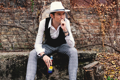 Mid adult man with fedora hat thinking while drinking beer and relaxing outdoors.