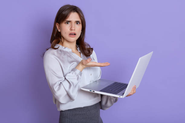 istock Young European woman frustrated by computer operational problems, looking at camera with puzzled and astonished expression, has unexpected troubles, pointing at laptop screen with palm. 1300330971