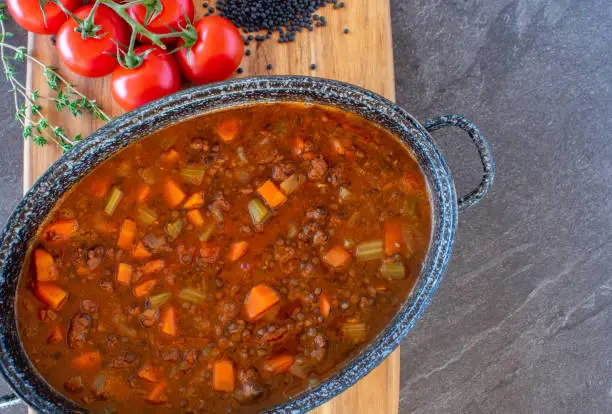 fresh cooked moroccan lentil soup with minced meat and vegetables served in a pot on wooden board from above with copy space