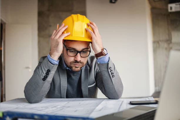 istock Focused architect holding his head, sights and looking at blueprints. Something got wrong. 1300334869
