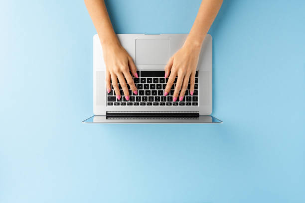 istock Overhead shot of woman’s hands using laptop on blue table. Office desktop. Flat lay 1300334975