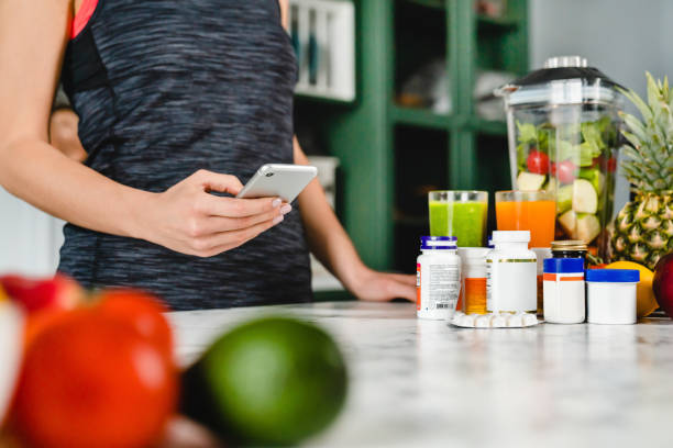 Young woman searching info about food supplements on her phone with fruits and additives on the table Young woman searching info about food supplements on her phone with fruits and additives on the table food additive stock pictures, royalty-free photos & images