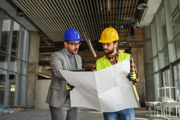 istock Construction worker holding blueprints and listening to suggestions architect talking about. 1300335352