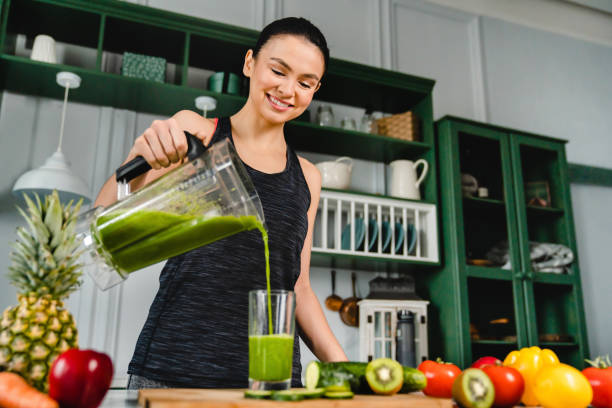 istock Happy young slim girl making fresh organic smoothie using blender in the kitchen 1300335968