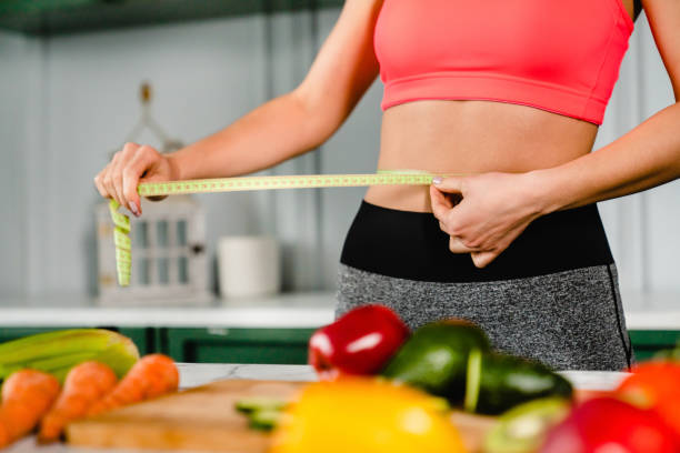 Healthy fit girl measuring her waist with measuring tape in the kitchen stock photo