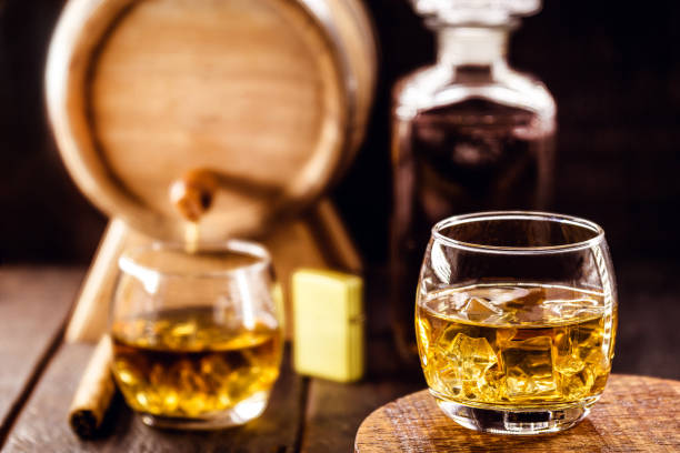 istock whiskey glass with ice, spot focus, bottle, lighter and barrel on blurred background. Distilled drink with malt 1300336807